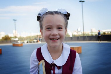 Güzel bir üniforma giyen, gülümseyen ve dışarıda gülen sevimli küçük bir okul kızının yakın plan portresi. Okul konseptine dönelim..