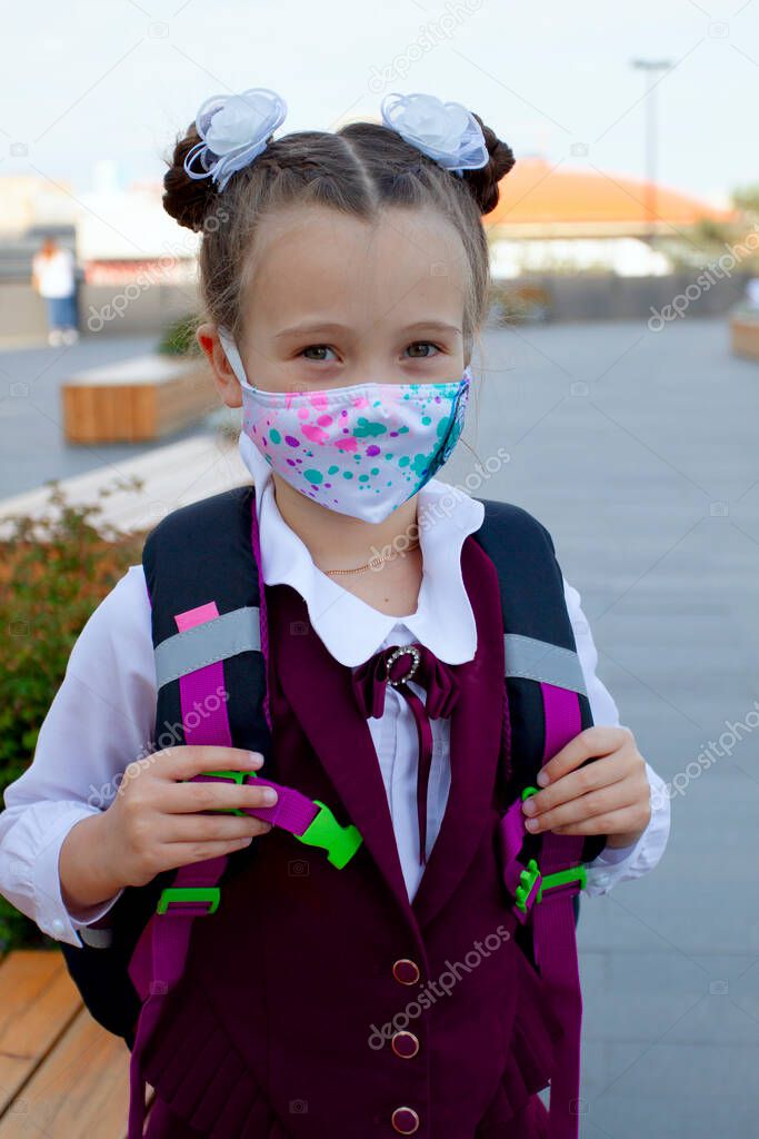 Little school girl wearing uniform and protection mask near the school outdoors. New normal. Coronavirus protection