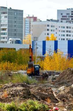İnşaat: büyük bir inşaat sahasının ortasında turuncu kazıcı, çukurlar, çöpler. Şehir inşaatı.