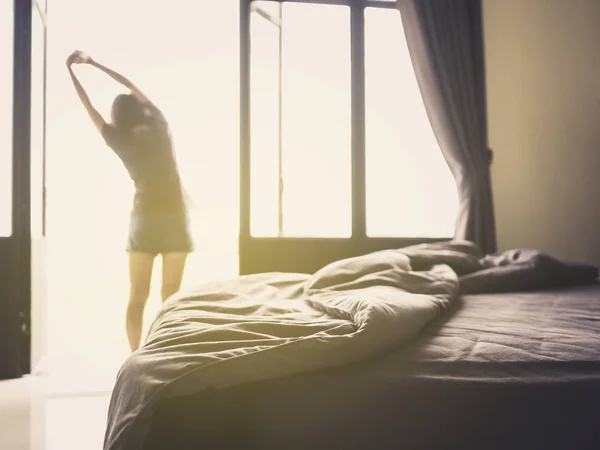 Confusion duvet and bed in luxury bedroom and healthy young woman stretching and relaxing by the window after waking up in the morning of holiday. Selective focus.