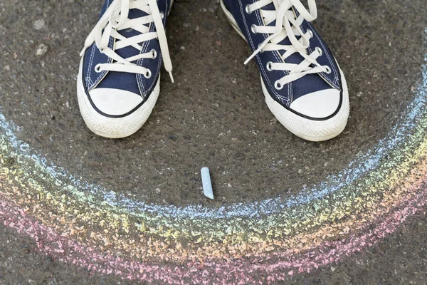 Feet in sneakers are on asphalt before drawn a rainbow