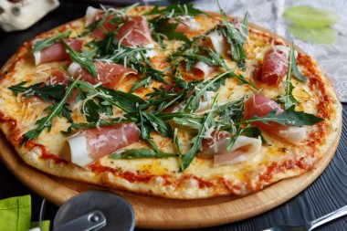 Siyah ahşap arka plan üzerinde ahşap bir çanak üzerinde pastırma, peynir ve otlar ile Pizza