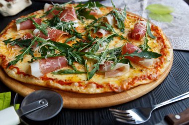 Siyah ahşap arka plan üzerinde ahşap bir çanak üzerinde pastırma, peynir ve otlar ile Pizza