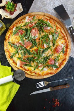 Siyah ahşap arka plan üzerinde ahşap bir çanak üzerinde pastırma, peynir ve otlar ile Pizza