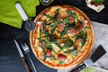 Siyah ahşap arka plan üzerinde ahşap bir çanak üzerinde pastırma, peynir ve otlar ile Pizza