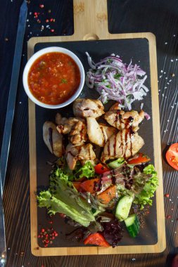 Siyah ahşap arka plan üzerinde bir kesme tahtası üzerinde domates sosu ve yeşillik ile domuz kebap