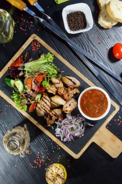 Siyah ahşap arka plan üzerinde bir kesme tahtası üzerinde domates sosu ve yeşillik ile domuz kebap