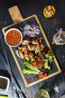 Siyah ahşap arka plan üzerinde bir kesme tahtası üzerinde domates sosu ve yeşillik ile domuz kebap
