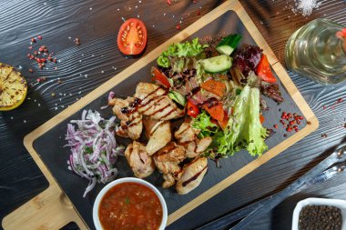 Siyah ahşap arka plan üzerinde bir kesme tahtası üzerinde domates sosu ve yeşillik ile domuz kebap