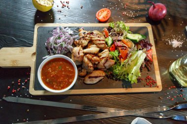 Siyah ahşap arka plan üzerinde bir kesme tahtası üzerinde domates sosu ve yeşillik ile domuz kebap