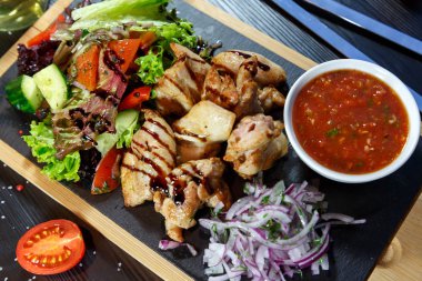 Siyah ahşap arka plan üzerinde bir kesme tahtası üzerinde domates sosu ve yeşillik ile domuz kebap