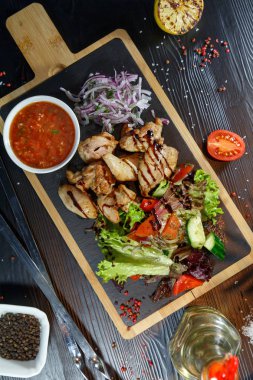 Siyah ahşap arka plan üzerinde bir kesme tahtası üzerinde domates sosu ve yeşillik ile domuz kebap