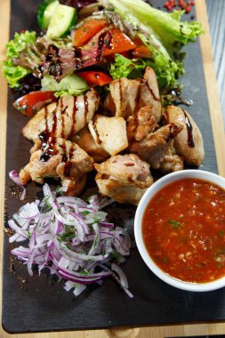 Siyah ahşap arka plan üzerinde bir kesme tahtası üzerinde domates sosu ve yeşillik ile domuz kebap