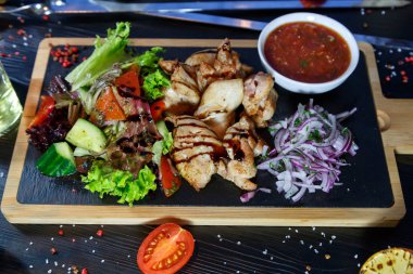 Siyah ahşap arka plan üzerinde bir kesme tahtası üzerinde domates sosu ve yeşillik ile domuz kebap