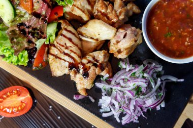 Siyah ahşap arka plan üzerinde bir kesme tahtası üzerinde domates sosu ve yeşillik ile domuz kebap