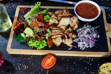 Siyah ahşap arka plan üzerinde bir kesme tahtası üzerinde domates sosu ve yeşillik ile domuz kebap