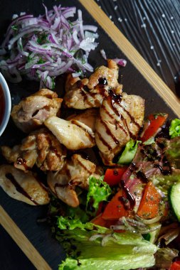 Siyah ahşap arka plan üzerinde bir kesme tahtası üzerinde domates sosu ve yeşillik ile domuz kebap