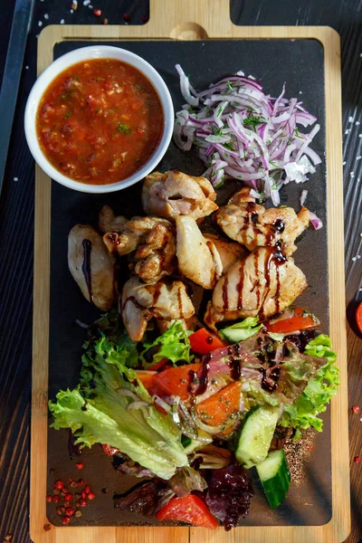 Siyah ahşap arka plan üzerinde bir kesme tahtası üzerinde domates sosu ve yeşillik ile domuz kebap