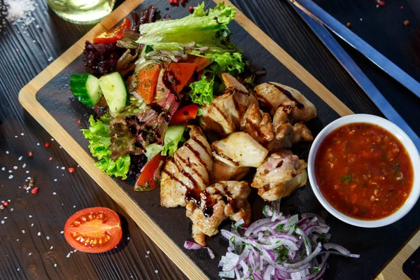 Siyah ahşap arka plan üzerinde bir kesme tahtası üzerinde domates sosu ve yeşillik ile domuz kebap
