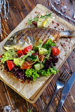 Kahverengi ahşap arka plan üzerinde mutfak tahtası üzerinde sebze ve otlar ile ızgara balık