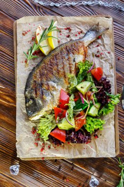 Kahverengi ahşap arka plan üzerinde mutfak tahtası üzerinde sebze ve otlar ile ızgara balık