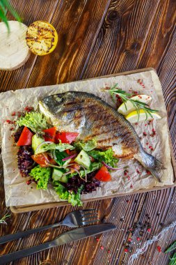 Kahverengi ahşap arka plan üzerinde mutfak tahtası üzerinde sebze ve otlar ile ızgara balık