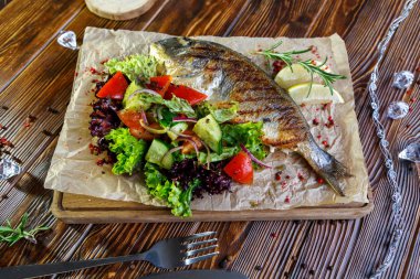 Kahverengi ahşap arka plan üzerinde mutfak tahtası üzerinde sebze ve otlar ile ızgara balık