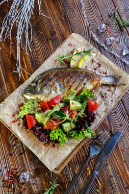 Kahverengi ahşap arka plan üzerinde mutfak tahtası üzerinde sebze ve otlar ile ızgara balık