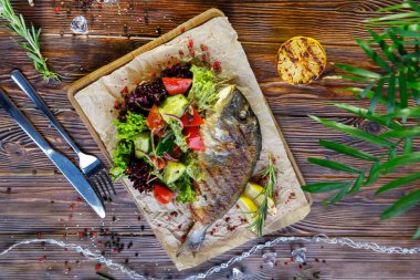 Kahverengi ahşap arka plan üzerinde mutfak tahtası üzerinde sebze ve otlar ile ızgara balık