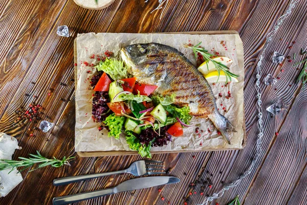 Grilled fish with vegetables and herbs on the kitchen board on a brown wooden background