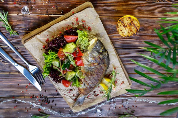 Kahverengi ahşap arka plan üzerinde mutfak tahtası üzerinde sebze ve otlar ile ızgara balık