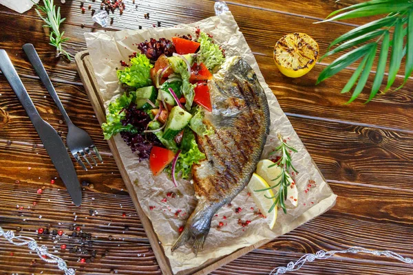 Grilled fish with vegetables and herbs on the kitchen board on a brown wooden background