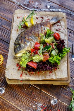 Kahverengi ahşap arka plan üzerinde mutfak tahtası üzerinde sebze ve otlar ile ızgara balık