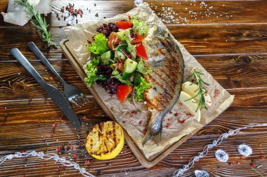 Kahverengi ahşap arka plan üzerinde mutfak tahtası üzerinde sebze ve otlar ile ızgara balık