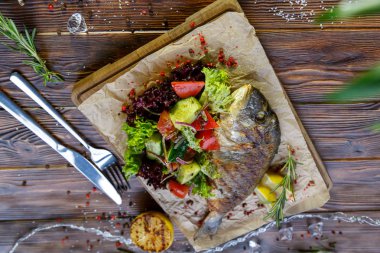 Kahverengi ahşap arka plan üzerinde mutfak tahtası üzerinde sebze ve otlar ile ızgara balık