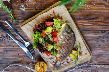 Kahverengi ahşap arka plan üzerinde mutfak tahtası üzerinde sebze ve otlar ile ızgara balık