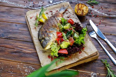 Kahverengi ahşap arka plan üzerinde mutfak tahtası üzerinde sebze ve otlar ile ızgara balık