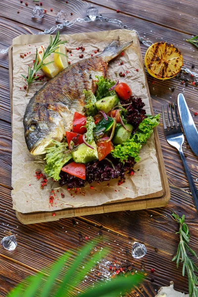 Grilled fish with vegetables and herbs on the kitchen board on a brown wooden background