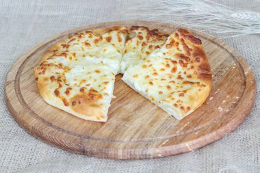 Çuval bezi arka planında tahta mutfak tahtasında peynirli Asya klasiği dilimlenmiş khachapuri tortilla.