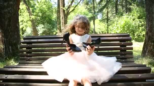 Little girl on the bench holding big shoes — Stock Video