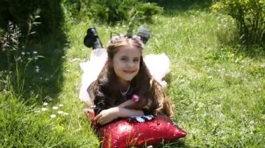 Küçük kız çimenlerin üstünde kırmızı bir yastık ile yatıyor.