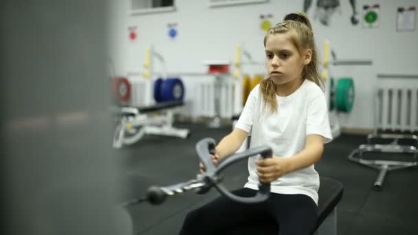 Chica colegiala en el gimnasio de entrenamiento en el simulador — Vídeo de stock