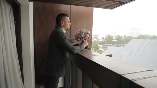 Ženich stojí na balkóně s kyticí v ruce. — Stock video