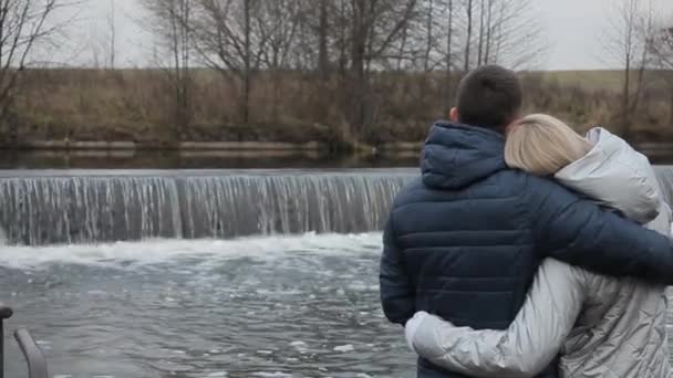 El chico y la chica se abrazaron en la naturaleza y miran la cascada — Vídeo de stock
