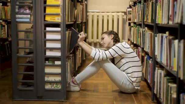 Menina sentada no chão e escolher um livro — Vídeo de Stock
