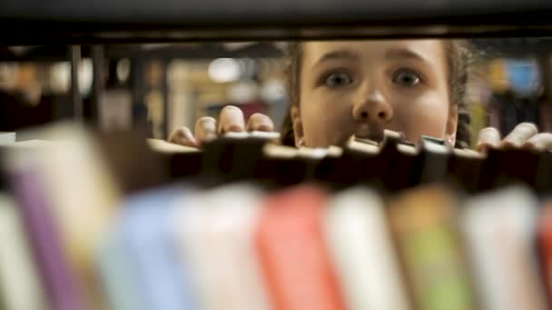 Chica mira por detrás de los libros — Vídeos de Stock
