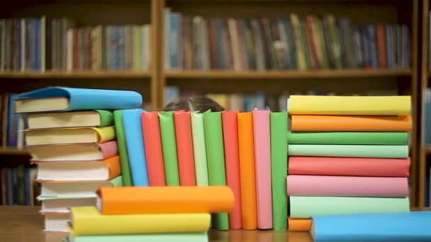 Una joven abraza una pila de libros en el fondo de estantes con libros — Vídeo de stock