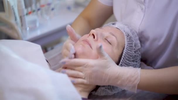 En la oficina de un cosmetólogo, una mujer tiene 40 años de edad en los procedimientos. Masaje facial — Vídeo de stock