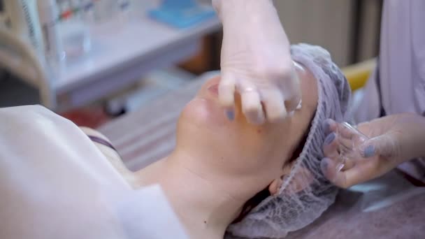 A beautician in gloves puts a transparent gel on the face of a young woman. — Stock Video