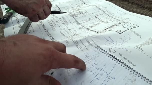 Архитектор и инженер-строитель проверяют план здания, сравнивают точные размеры чертежа и пишут в блокноте — стоковое видео